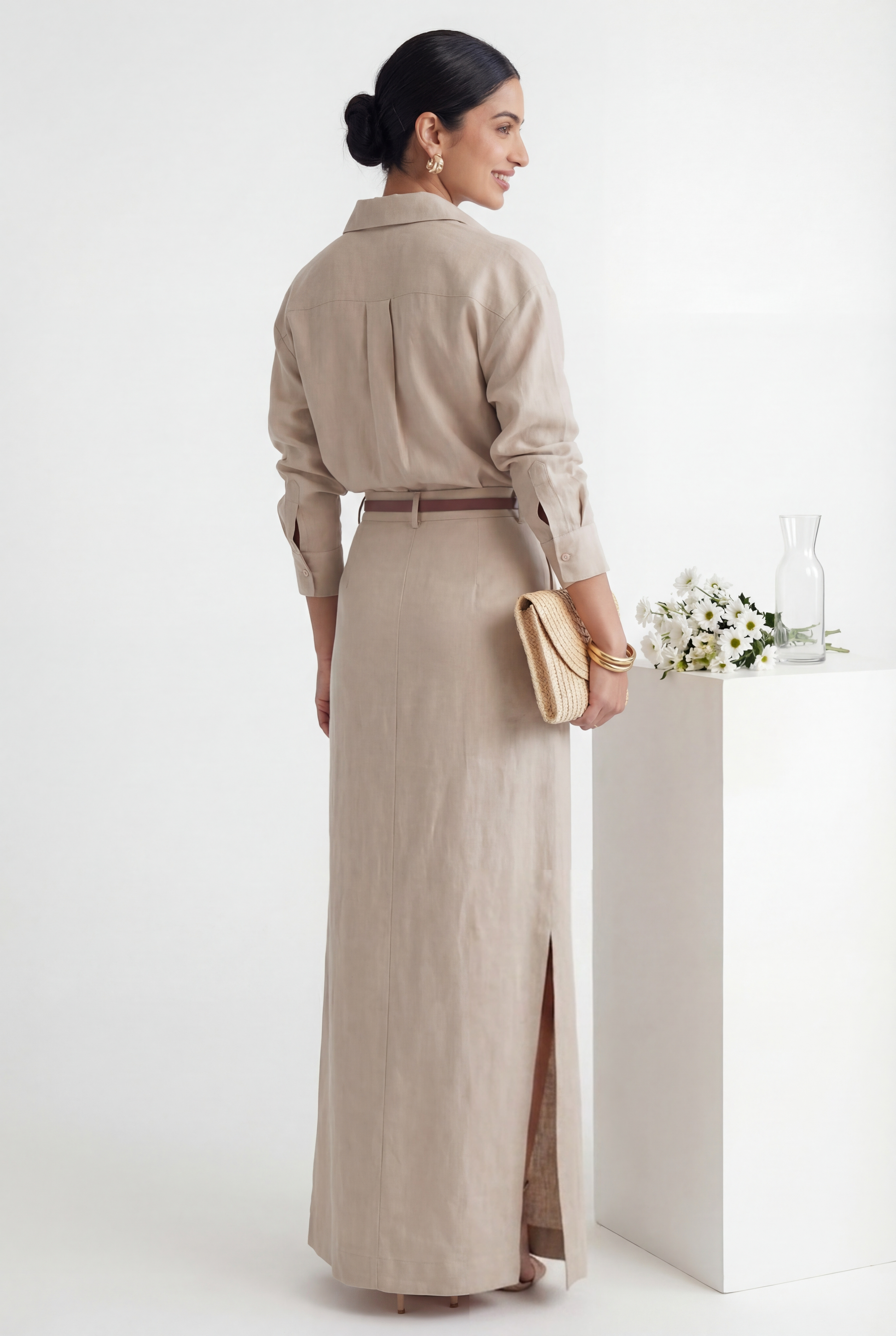 Woman in a beige dress standing next to a white podium with flowers on a white background