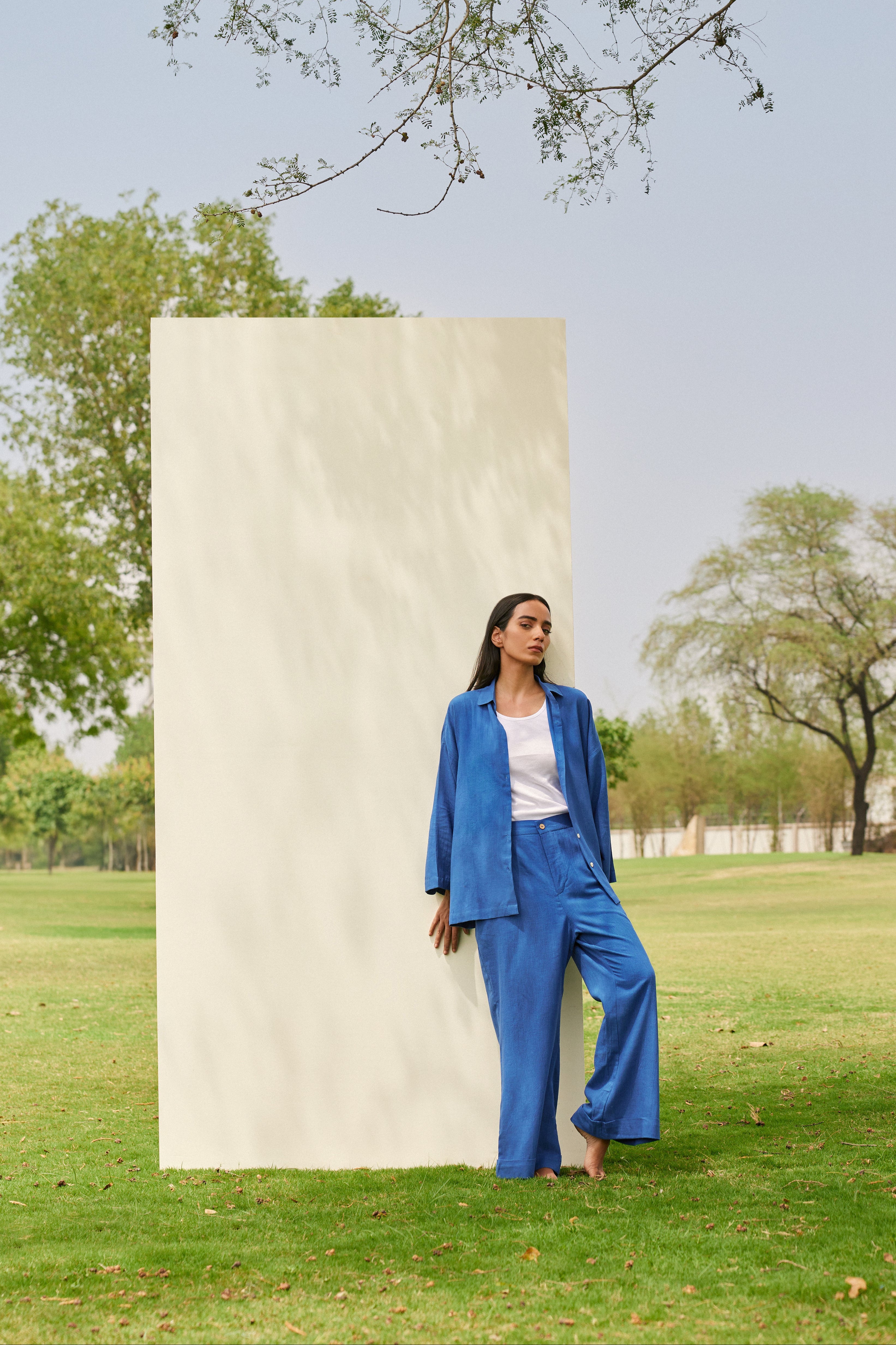 Woman in a blue suit standing next to a tall rectangular sculpture in a park.