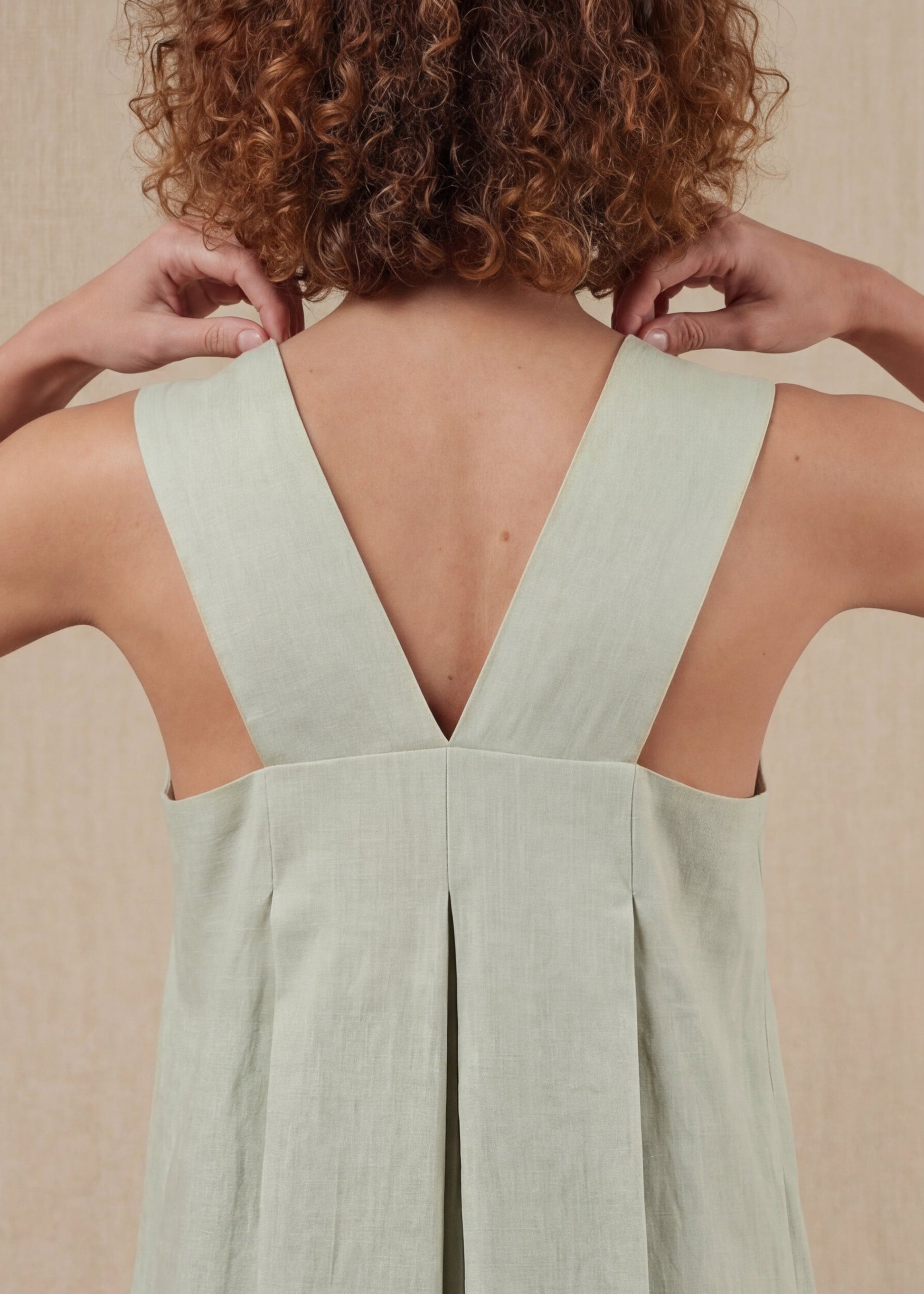 Person wearing a light green dress with a V-neckline against a beige background