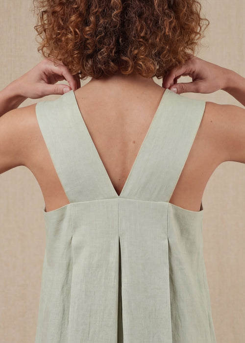 Person wearing a light green dress with a V-neckline against a beige background