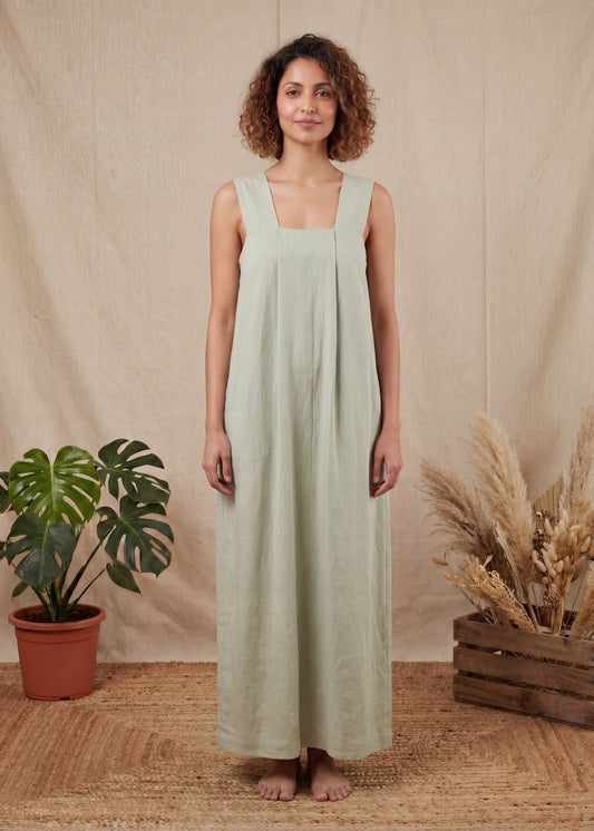 Woman wearing a light green dress standing in front of a beige curtain with plants on either side.