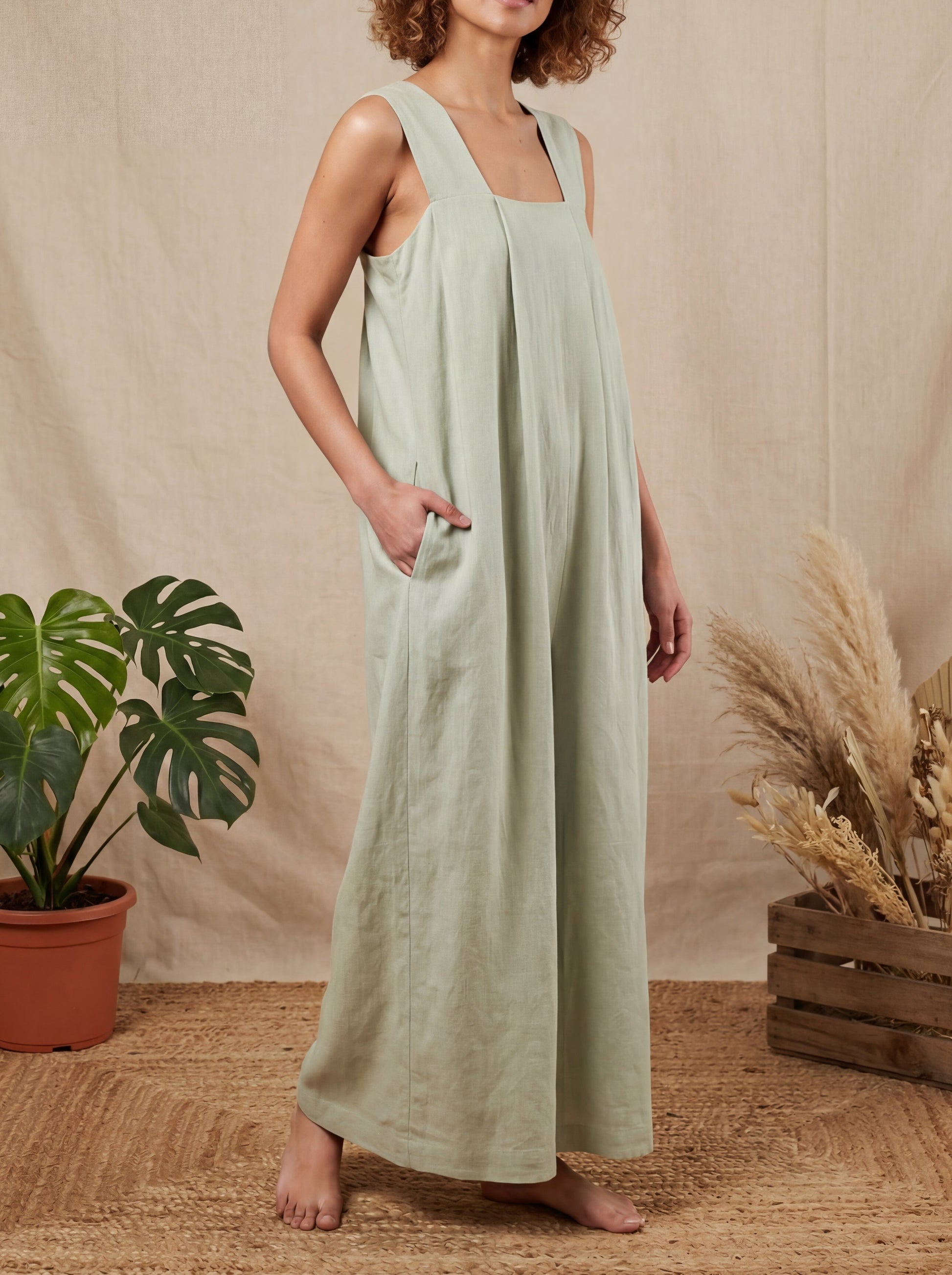 Woman wearing a light green dress standing in front of a beige wall with plants.